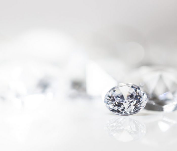 Diamant auf weiß mit Spiegelung vor weißem Hintergrund, mehrere Diamanten in der Unschärfe, Edelsteine mit Textfreiraum